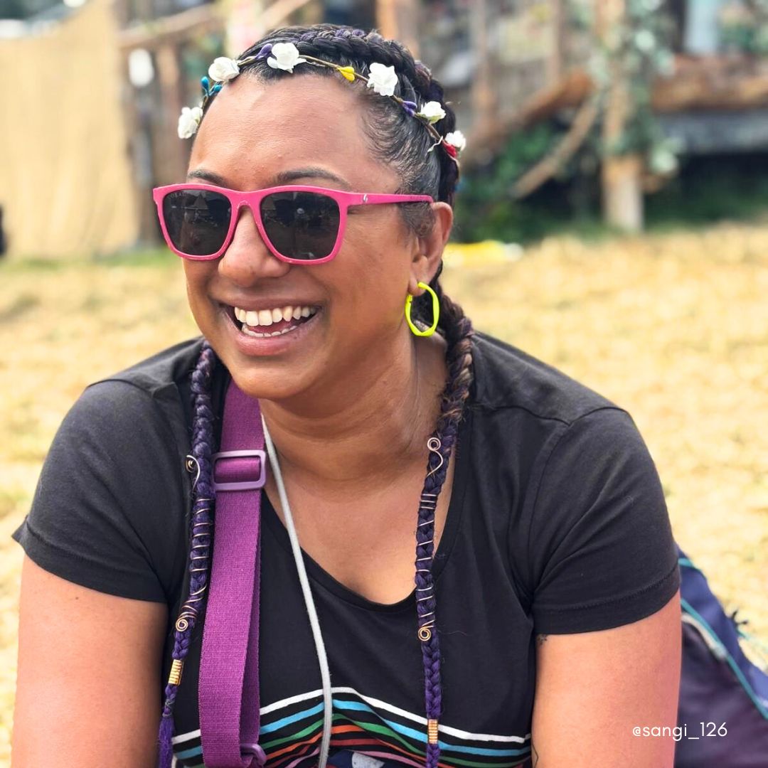 Woman wearing neon yellow hoop earrings, a flower garland in her hair and pink sunglasses at Glastonbury.
