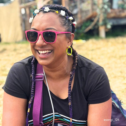 Woman wearing neon yellow hoop earrings, a flower garland in her hair and pink sunglasses at Glastonbury.